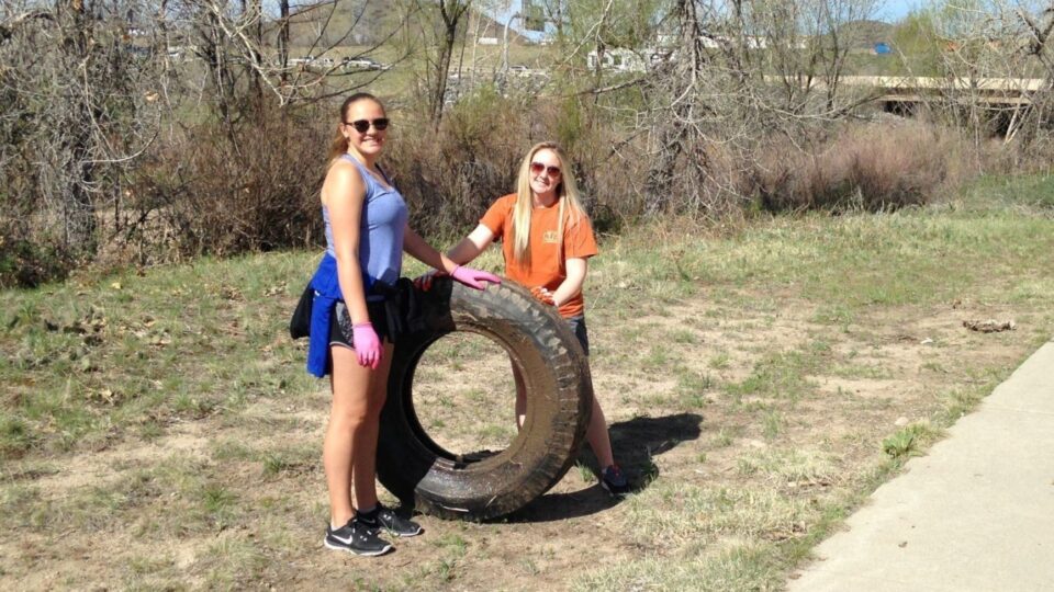 Two people removing a large tractor tire from the creek