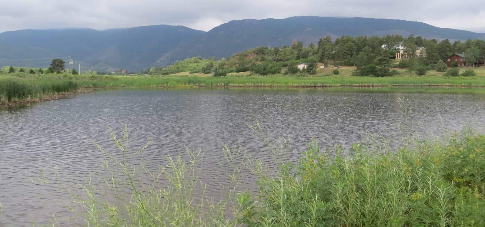 View of the Gateway Pond in Perry Park with mountains in the background on a cloudy day